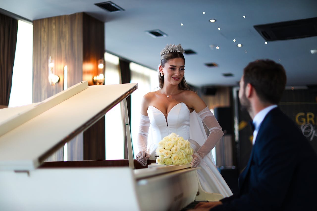 Bride in elegant gown by grand piano during a wedding ceremony indoors.